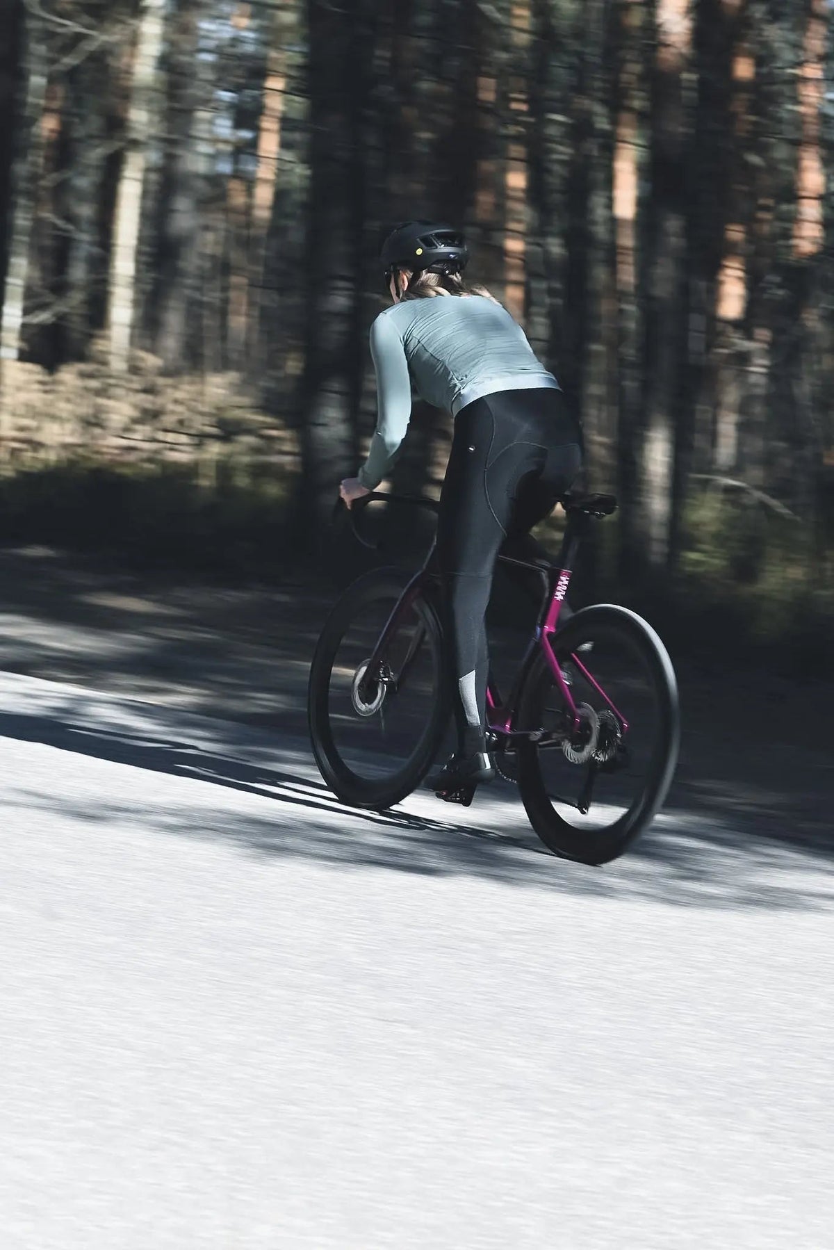 Cyclist riding an IKUISTA road bike along a forest road, rear three-quarter view