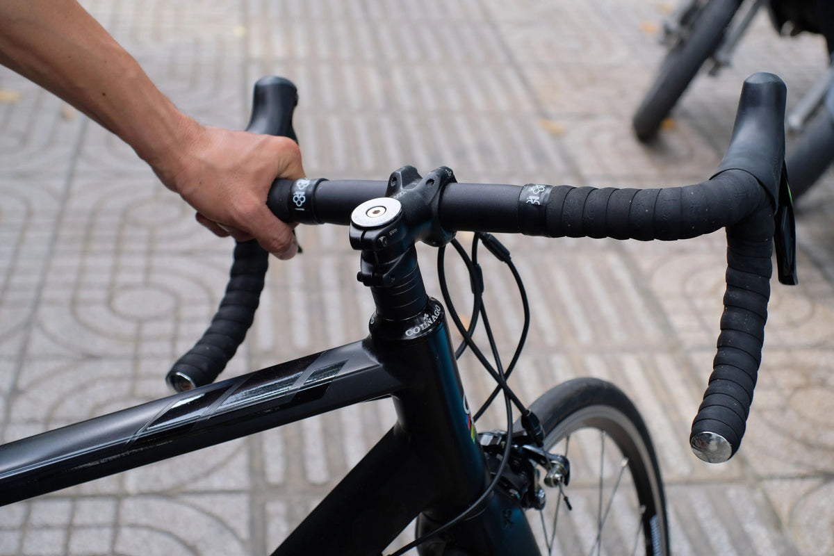 Close-up of a cyclist's hand on drop-bar handlebars and stem, urban street in the background